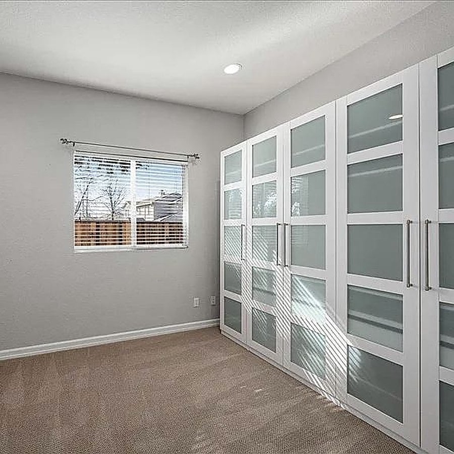 Before: carpeted spare bedroom with a window and frosted-glass closet doors